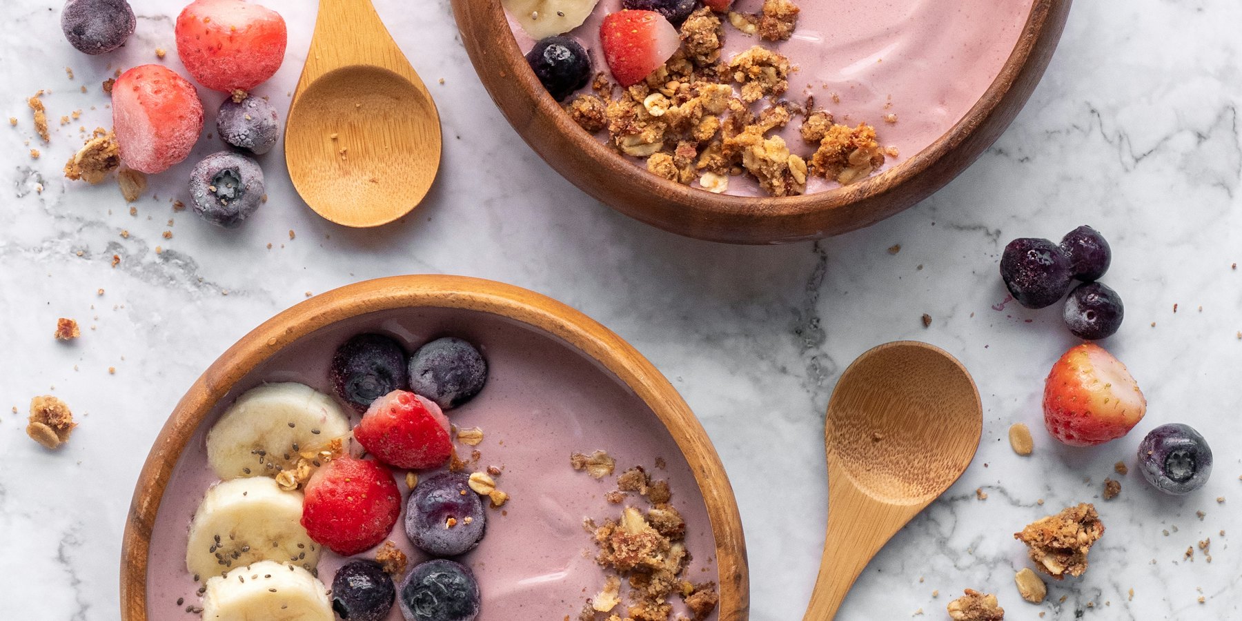 Two smoothie bowls with fruit and granola on a marble table